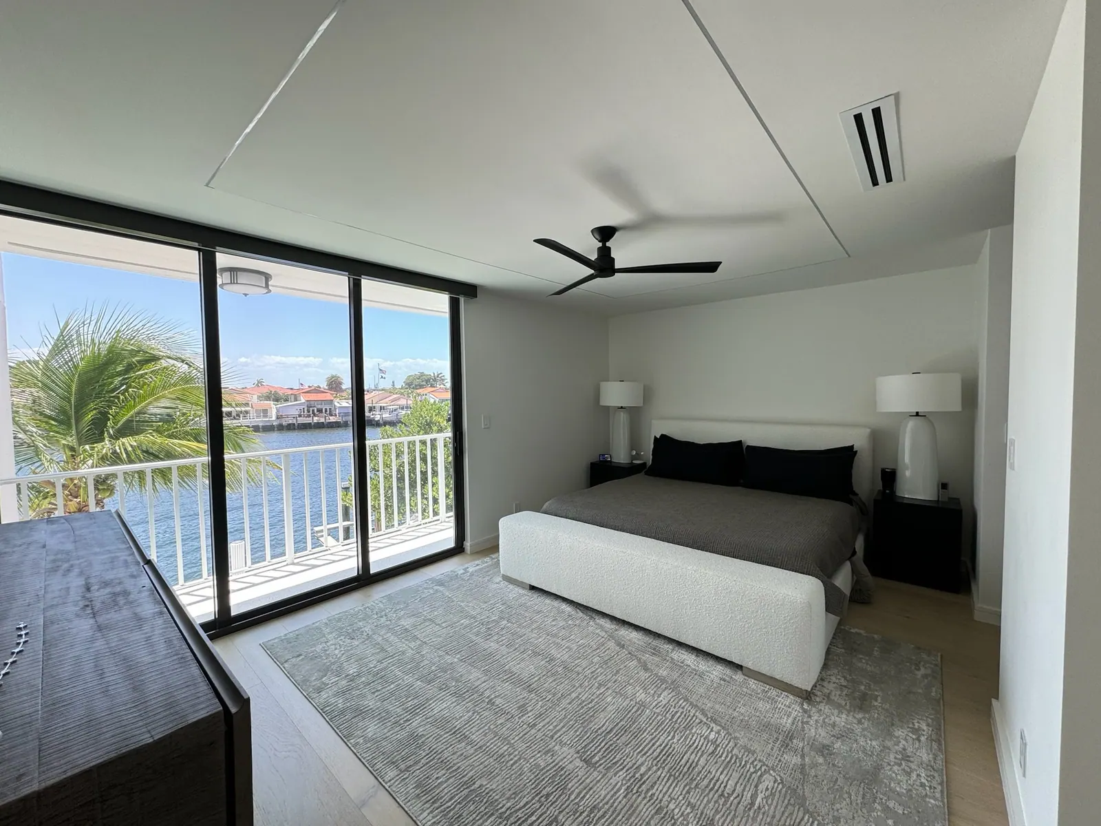 After: Primary bedroom with wide plank flooring opening to a waterfront balcony